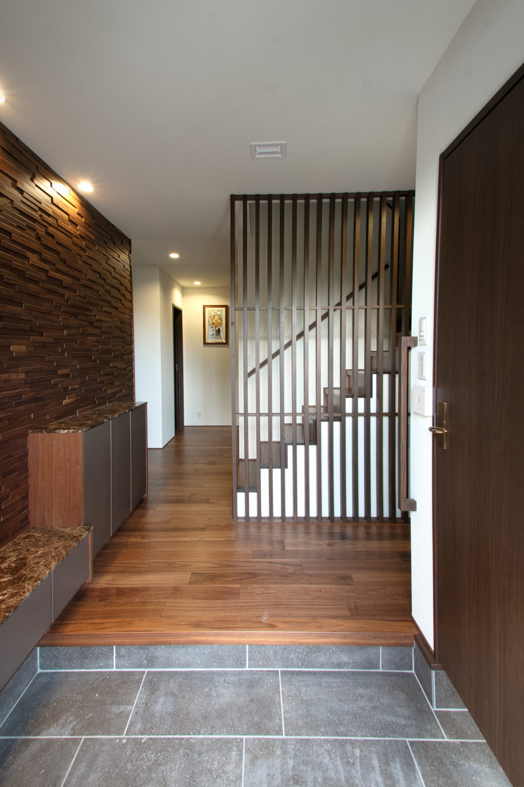 広々とした玄関は階段横の壁を格子パネルとしてさらに視線の抜ける空間に大きな壁面の木調パネルが存在感を醸し出します。